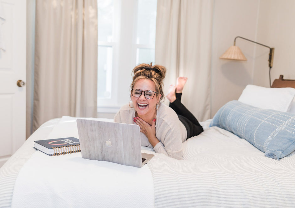 Sierra Friend laughing on a bed with her laptop, feet raised and planners beside her